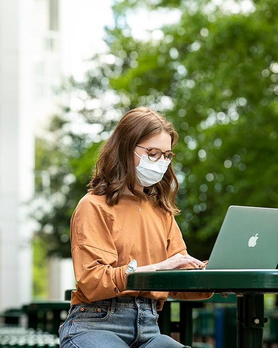 Female student works outdoors on Mason's Fairfax Campus. Masks are required in all public spaces.