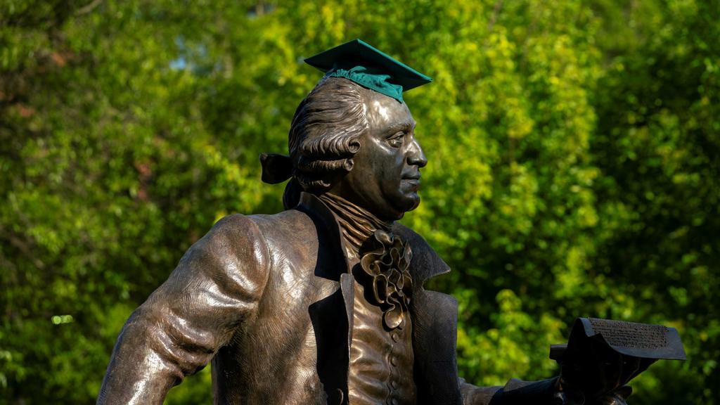 The George Mason statue wears a green graduation cap.