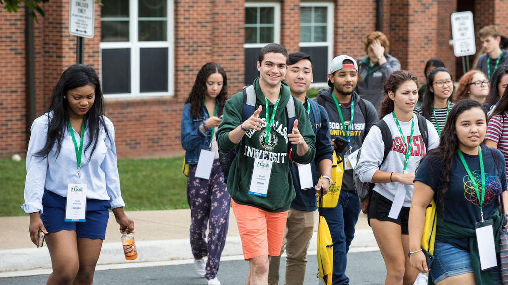 A young person points at the camera and smiles while walking with a group on Mason's campus.