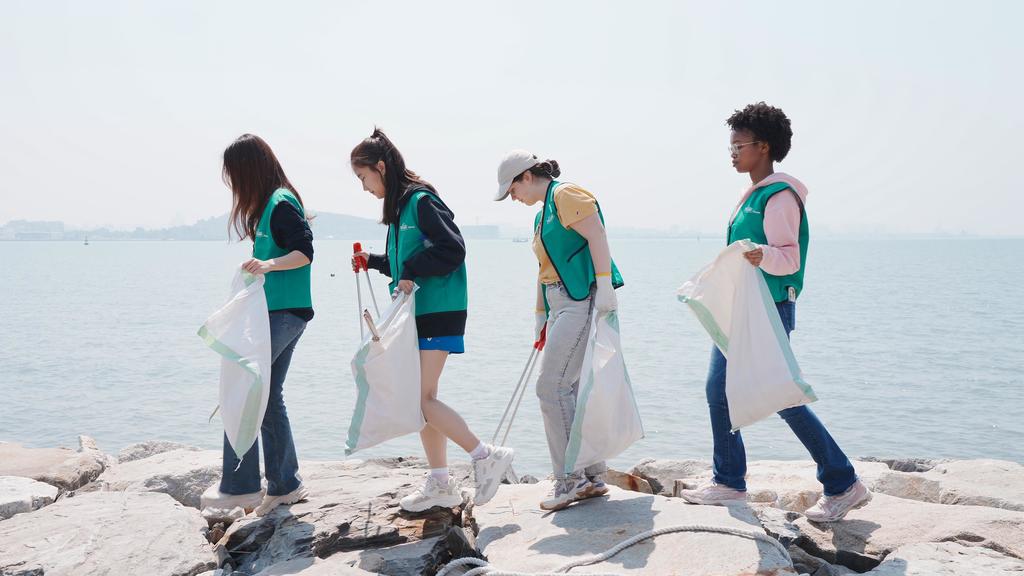 Four Mason Korea students wearing green Mason Cares vests pick up trash along the beach.
