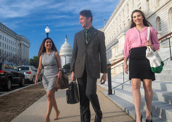 Professionals walking down the steps of a building with the dome of the US Capitol in the background.